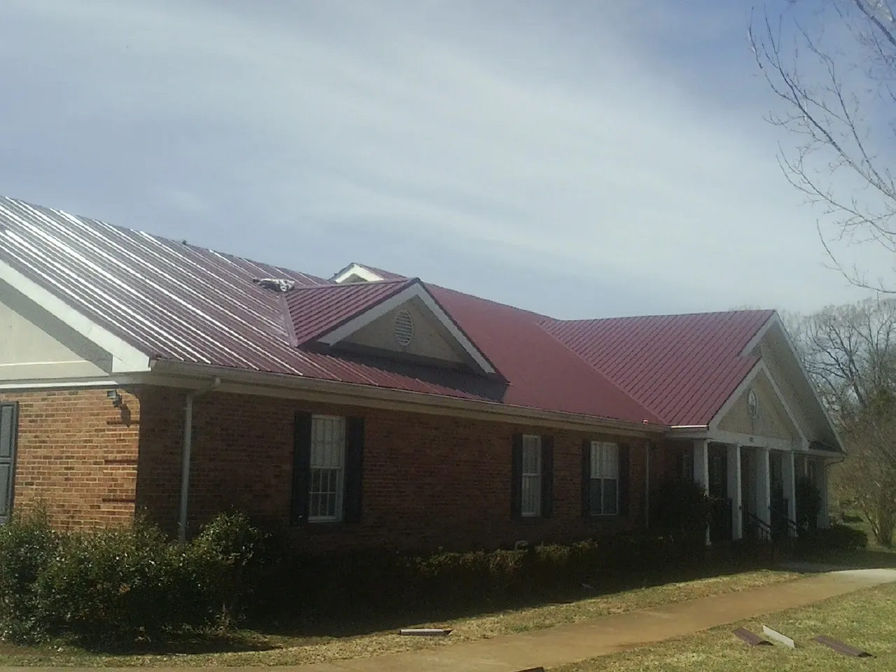 Red metal roof with gabled entries on a long brick building, from a Hail Damage Roof Repair job in Herndon